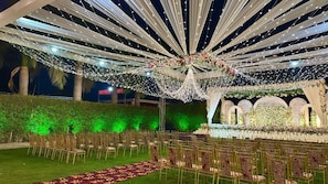 An outdoor event space with rows of chairs, a decorated stage, and string lights.