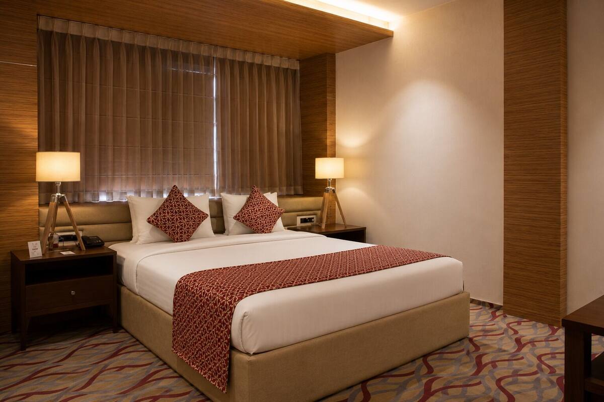 Una habitación de hotel con una cama grande, dos mesitas de noche, una lámpara y un ventanal con cortinas.