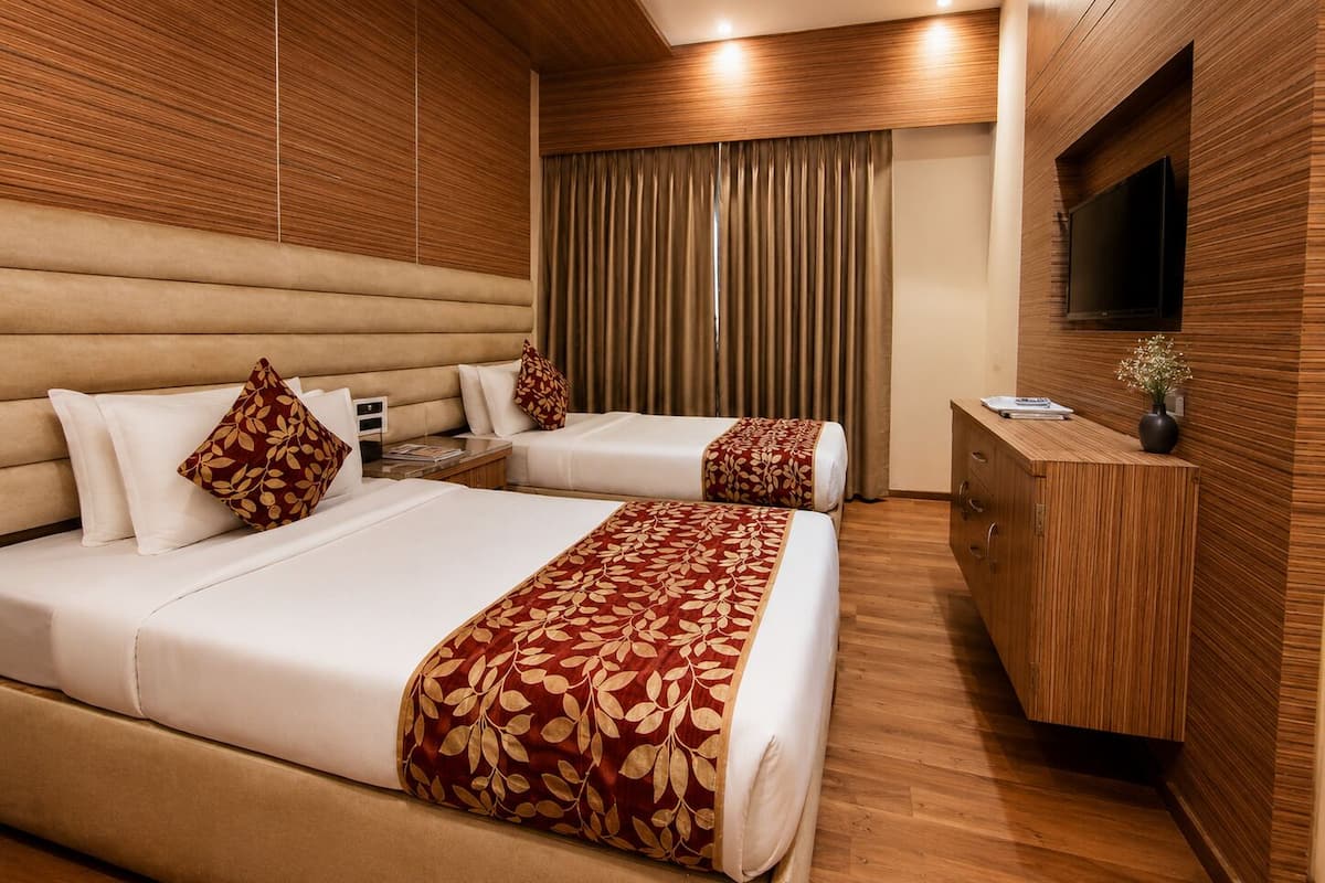 A hotel room with two beds, a wooden headboard, a flat-screen TV, and a wooden desk.
