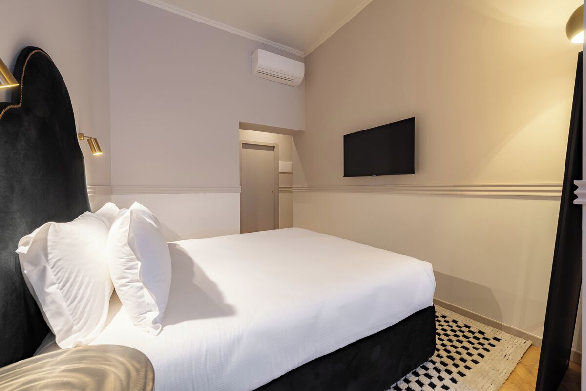 Habitación de hotel con cama, televisor de pantalla plana montado en la pared, aire acondicionado y alfombra estampada.