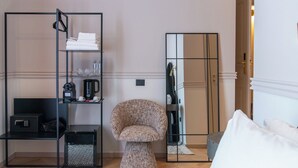 Een hotelkamer met een spiegelkast, een rond gestoffeerde fauteuil, een klein bijzettafeltje en een bed met wit beddengoed.