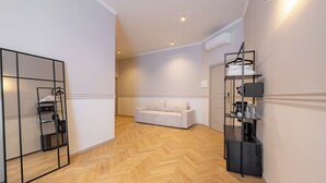 Een hotelkamer met een visgraatvloer, een witte bank, een spiegelkast en een zwart wandrek met een koffiezetapparaat.