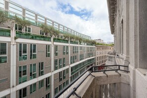Um edifício moderno com vários andares, com grandes janelas e uma varanda com vegetação.
