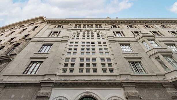 Een groot gebouw met een symmetrische gevel, boogvensters en een middenstuk met een rasterpatroon.
