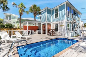Ein zweistöckiges Haus mit Swimmingpool, Gartenmöbeln und einer Palme.