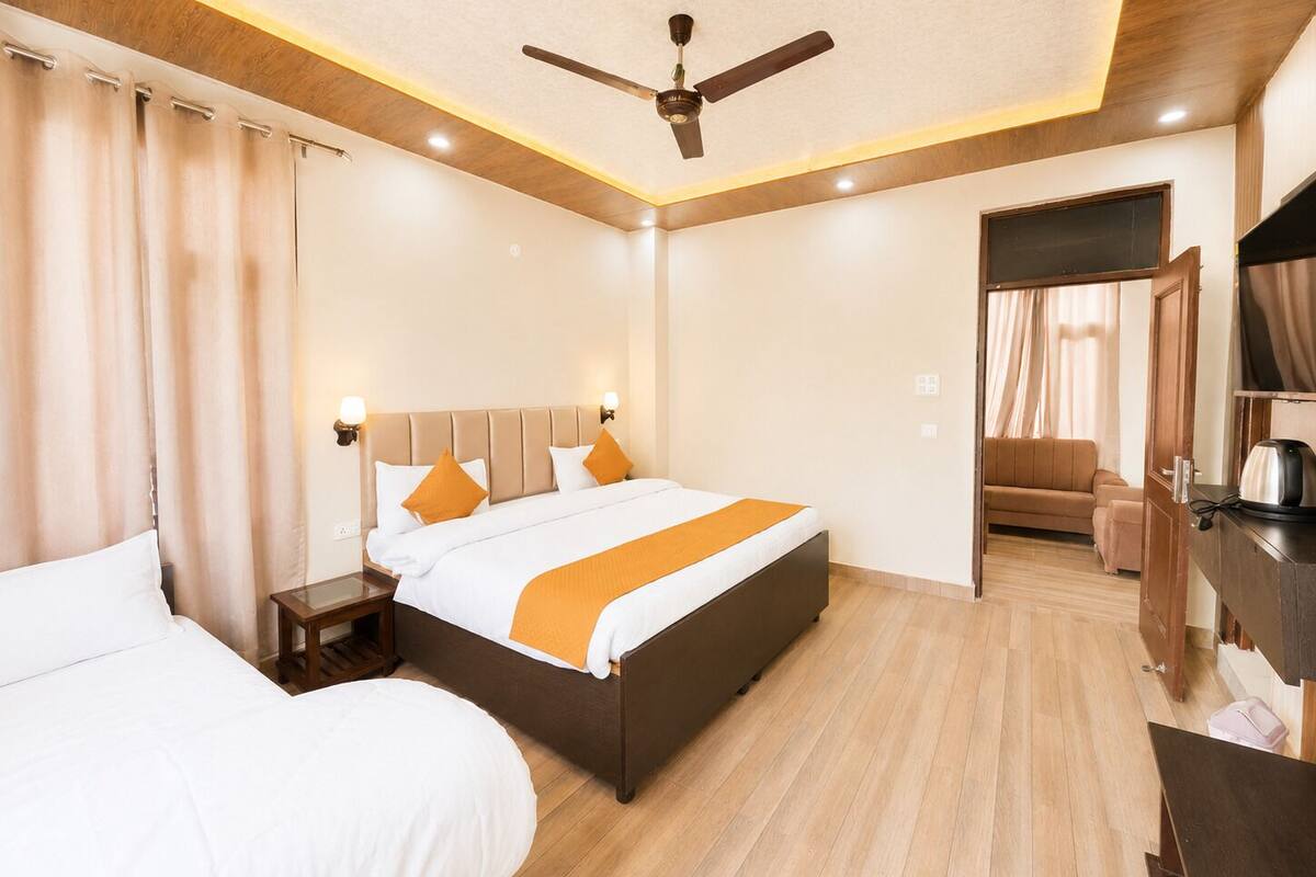 A hotel room with a bed, bedside tables, a ceiling fan, a sofa, and a desk with a kettle.