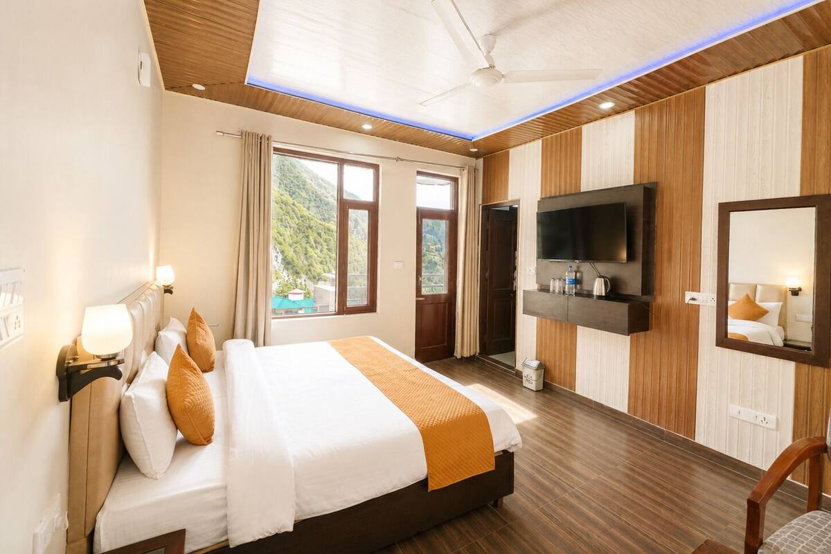 A hotel room with a bed, a TV, a mirror, and a window with a view of greenery.