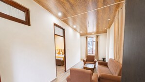 Ein Hotelzimmer mit Holzboden, einer Couch, einem Sessel, einem kleinen Tisch und einem Bett, das durch eine geöffnete Tür zu sehen ist.