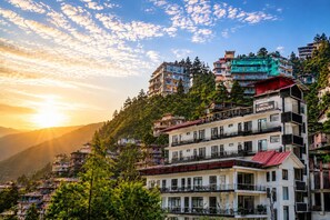 A hotel with multiple floors, balconies, and a view of the surrounding mountainous landscape. - Hotel Sarovar Mcleodganj At Bhagsu Chowk (Dharamshala)