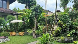 A lush garden with a pathway, two wooden chairs, and a thatched-roof structure. - Unique 1BR Villa Ubud Center (Ubud)