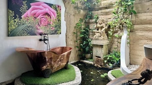 A rustic bathroom with a copper bathtub, a decorative wall with a rose painting, and a small garden area with plants and a stone sculpture. - Unique 1BR Villa Ubud Center (Ubud)