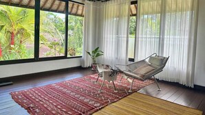 A room with a large window, a woven mat, a metal chair, and a potted plant. - Unique 1BR Villa Ubud Center (Ubud)
