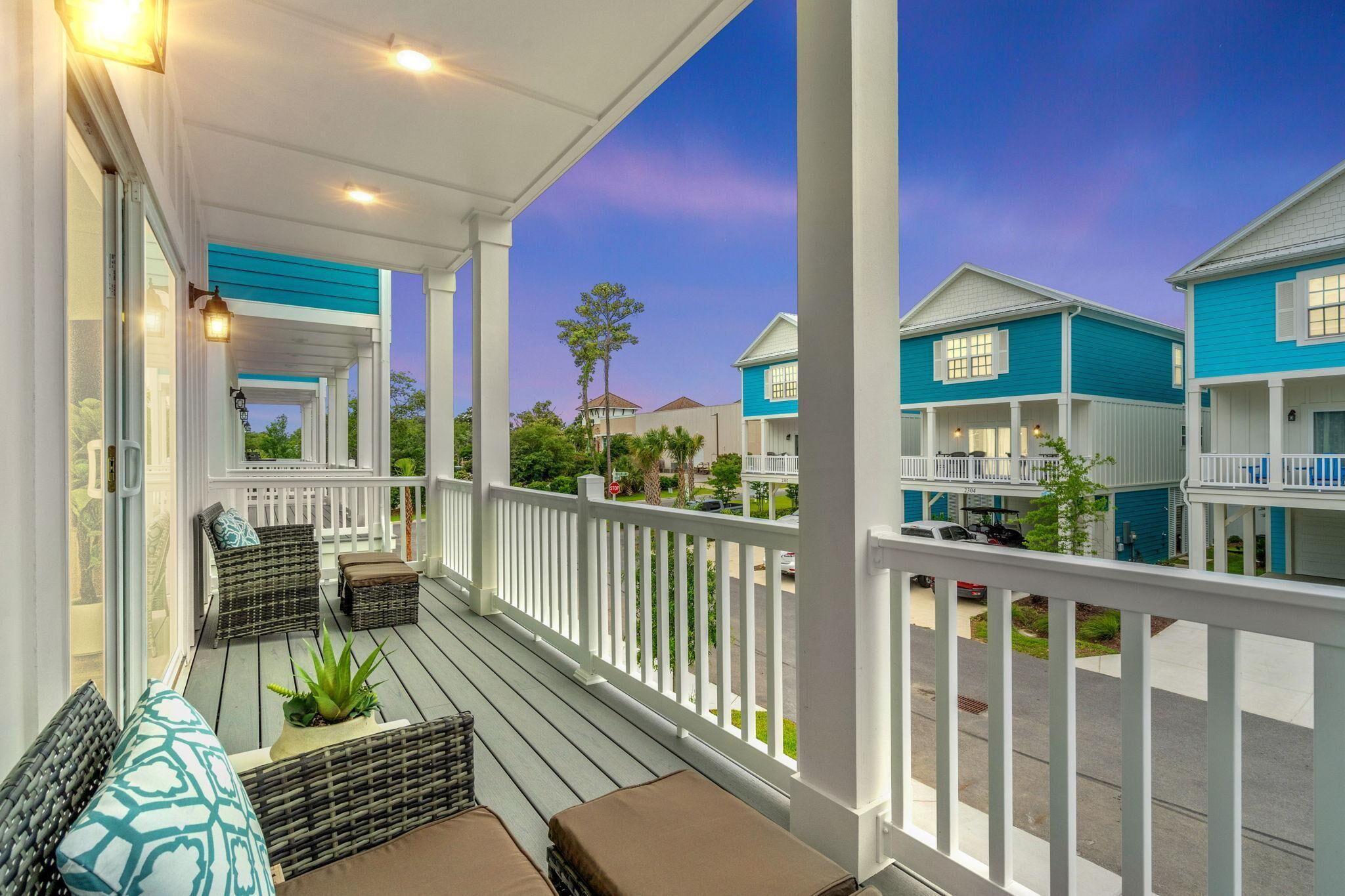 A covered porch with wicker furniture and a view of blue buildings.