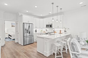 Una cocina moderna con armarios blancos, electrodomésticos de acero inoxidable y una isla central con taburetes de bar.