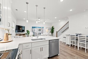 Una cocina moderna con armarios blancos, una isla central, electrodomésticos de acero inoxidable, iluminación colgante y vistas a un balcón.