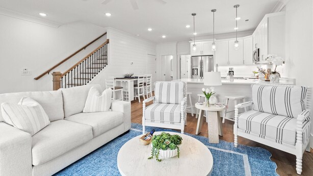 Ein modernes Wohnzimmer mit einem weißen Sofa, gestreiften Sesseln, einem Couchtisch mit einer Pflanze, einer Treppe und einer Küchenzeile.