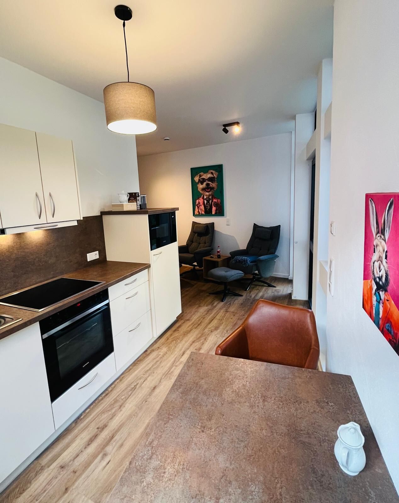 Une cuisine moderne avec un coin repas, un tableau représentant un chien accroché au mur et un tableau représentant un lapin.