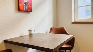 A dining area with a table, chairs, a painting, and a window.