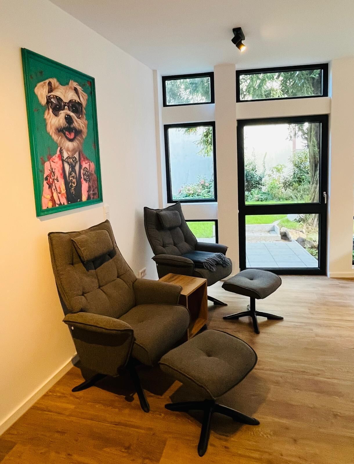 Ein modernes Wohnzimmer mit einem großen Fenster, einem grün gerahmten Gemälde eines Hundes und einem Holztisch.