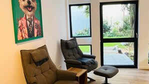 Uma sala de estar moderna com uma janela grande, um quadro com moldura verde retratando um cão, e uma mesa de centro de madeira.