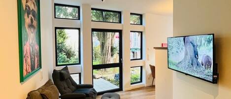 Una sala de estar moderna con un sofá modular, un televisor montado en la pared y grandes ventanales con vistas al exterior.