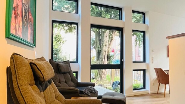 Uma sala de estar moderna com janelas amplas, um sofá, uma poltrona e uma mesinha.
