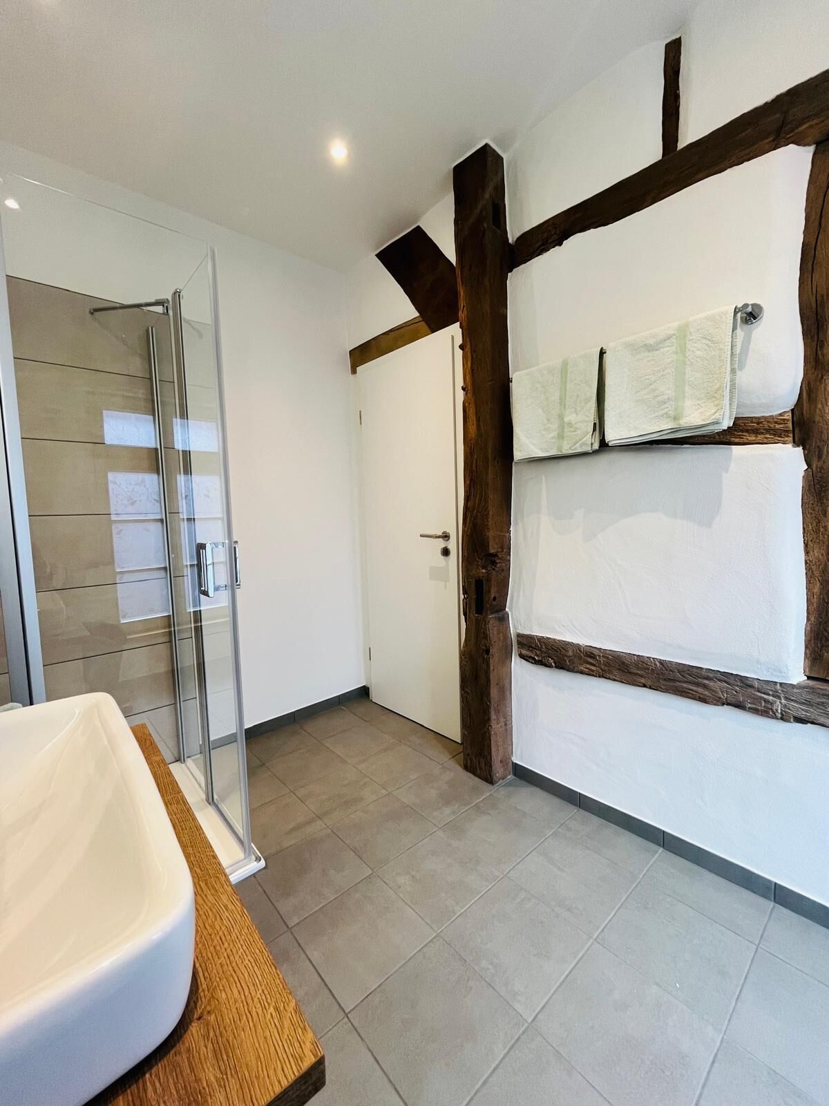 A bathroom with a glass shower enclosure, a white sink, and a wooden vanity.