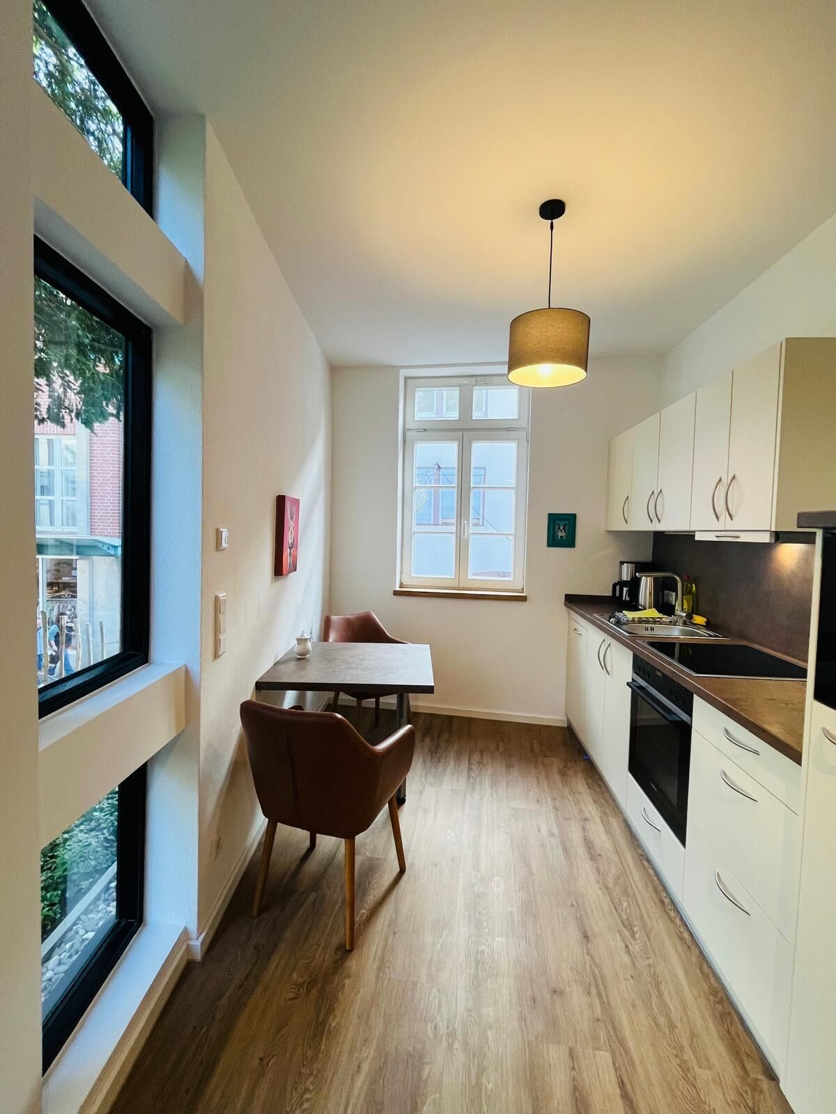 Een kleine keuken met een eettafel, stoelen, een hanglamp en een raam.