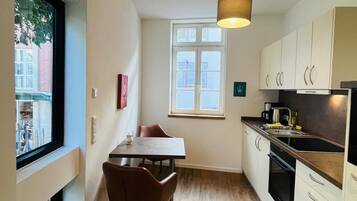Een kleine keuken met een eettafel, stoelen, een hanglamp en een raam.