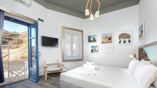 Un dormitorio con una cama, un televisor, una ventana con cortinas y cuadros en la pared.