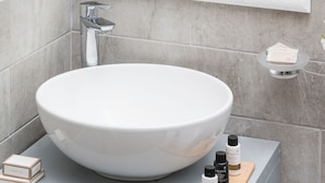 Un baño con un lavamanos blanco, un espejo y un estante pequeño con artículos de aseo.