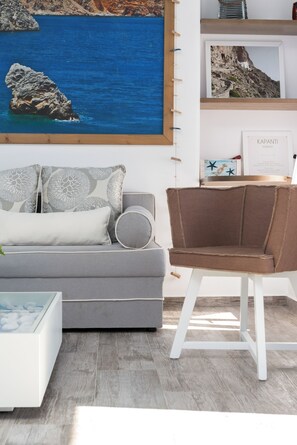 A modern living room with a grey sofa, a brown armchair, and a framed picture of a coastal landscape. - Sea View Apartment, Kaerati Apartments (Amorgos)