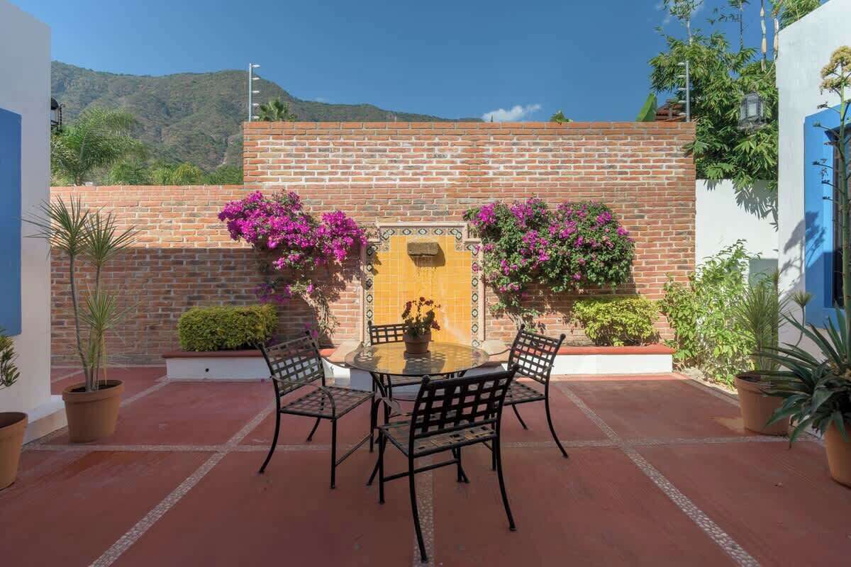 Un patio con una mesa redonda y cuatro sillas, un muro de ladrillo y plantas en macetas.