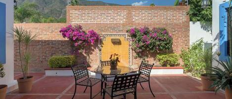 Un patio con una mesa redonda y cuatro sillas, un muro de ladrillo y plantas en macetas.