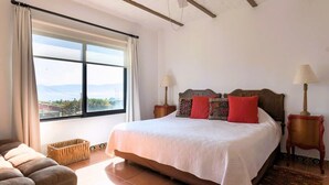 Un dormitorio con una cama grande, una ventana con cortinas, techo de madera y vistas al exterior.