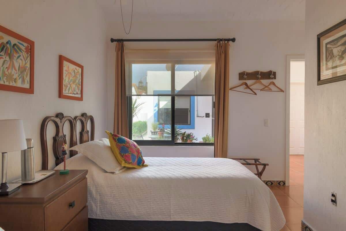 A bedroom with a bed, a nightstand, a window with curtains, and wall art.