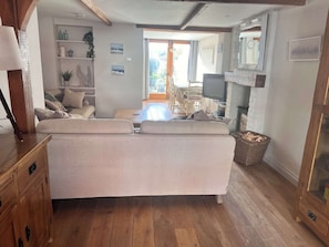Een gezellige woonkamer met een bank, houten vloer, een televisie en een open haard.