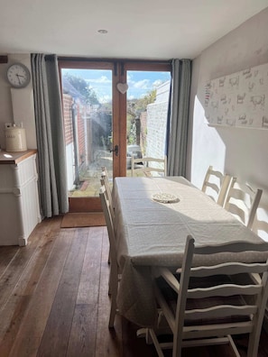 Een eetruimte met een tafel, stoelen, een klok en uitzicht door een glazen deur op een buitenruimte.