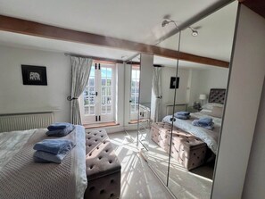 A bedroom with two beds, a large mirror, and a window with curtains. - 3 bedroom cottage with garden in Arundel (West Sussex)