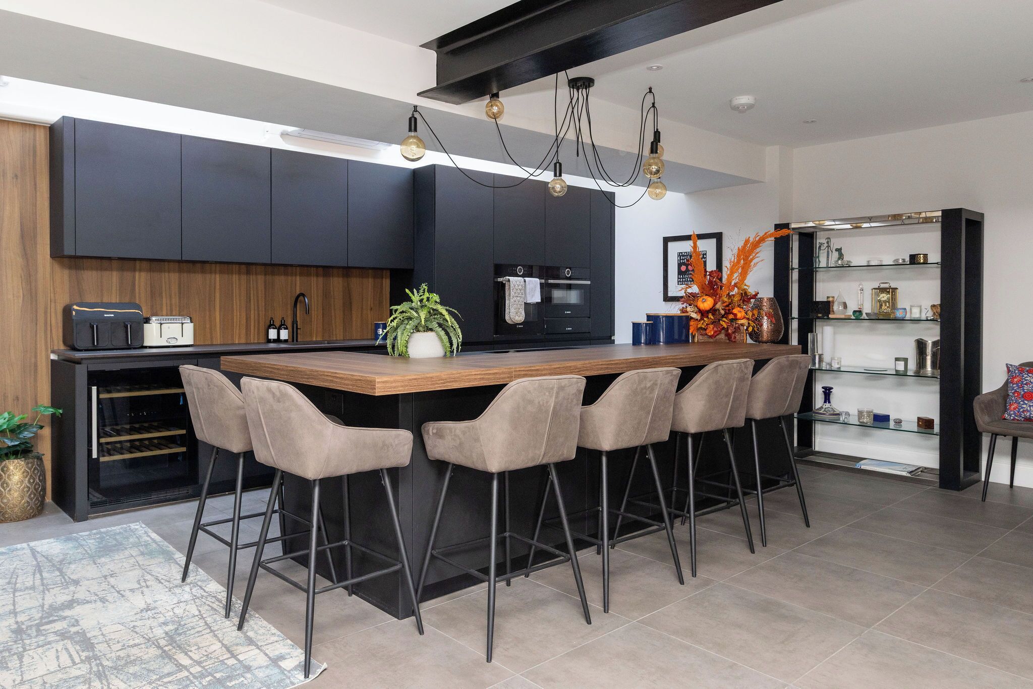A modern kitchen with a central island, bar stools, a wine rack, and a built-in oven.
