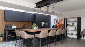 Eine moderne Küche mit einer zentralen Kochinsel, Barhocker, einem Weinkühlschrank und einem eingebauten Backofen.