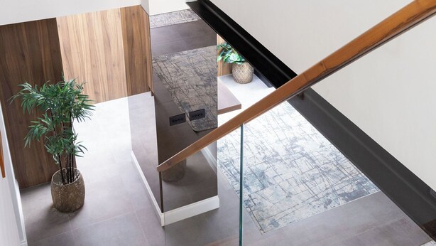 Eine moderne Treppe mit Holzboden und Glastrennwerken, die zu einem Zwischenpodest mit einem Blumentopf und einem kleinen Tisch führt.