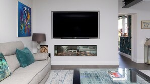 Ein Wohnzimmer mit Sofa, Flachbildfernseher, einem Gemälde und einem Kamin.