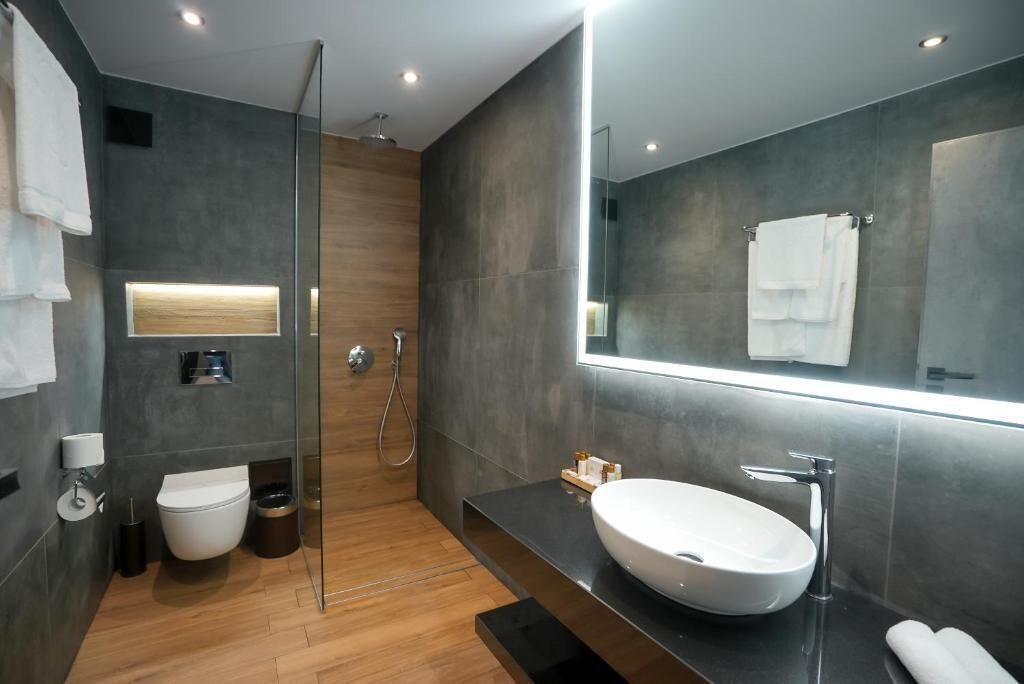 Een moderne badkamer met een glazen douchecabine, een witte wastafel en een grote spiegel.