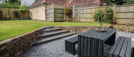 A backyard with a stone wall, a wooden deck, and a house with a red roof.
