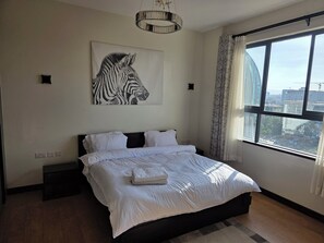 Ein Schlafzimmer mit einem großen Bett, einem Wandbild mit Zebra-Motiv, einem Fenster mit Blick auf Gebäude und einer Kandelaber.