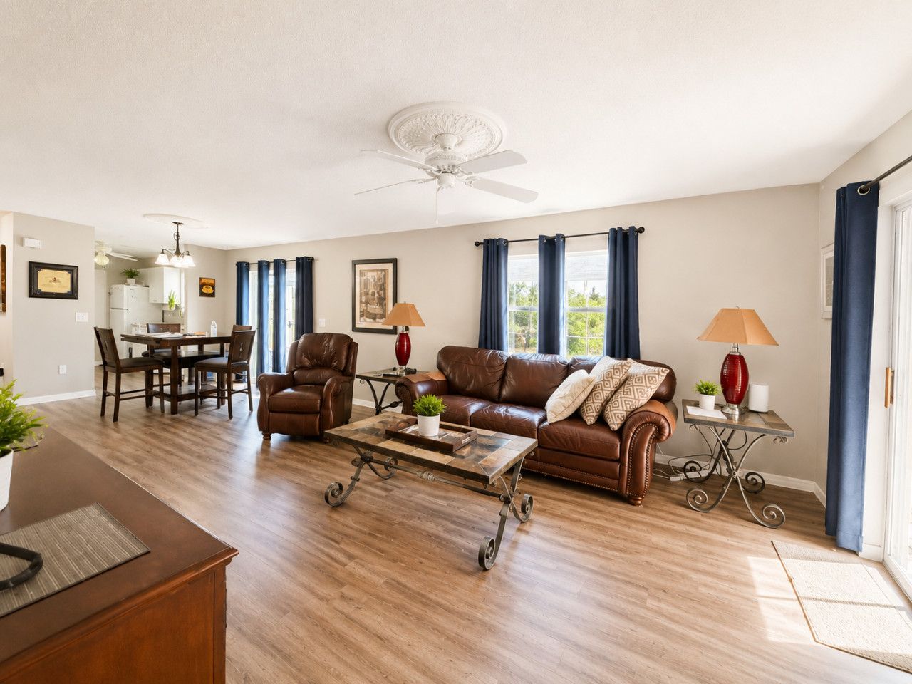 Ein Wohnzimmer mit braunem Ledersofa, einem Couchtisch, einem Essbereich mit Tisch und Stühlen sowie einem Deckenventilator.