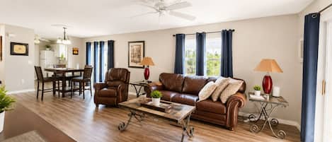 Ein Wohnzimmer mit braunem Ledersofa, einem Couchtisch, einem Essbereich mit Tisch und Stühlen sowie einem Deckenventilator.
