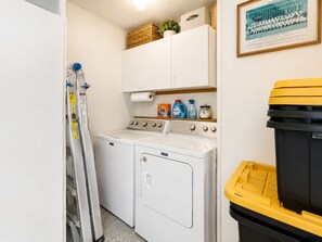 A laundry room with a washing machine, dryer, and stacked laundry baskets. - Alfredo Retreat at Spanish Springs (The Villages)