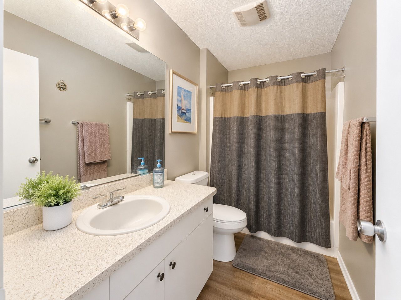 A bathroom with a double sink, a toilet, a shower curtain, a towel rack, and a potted plant.